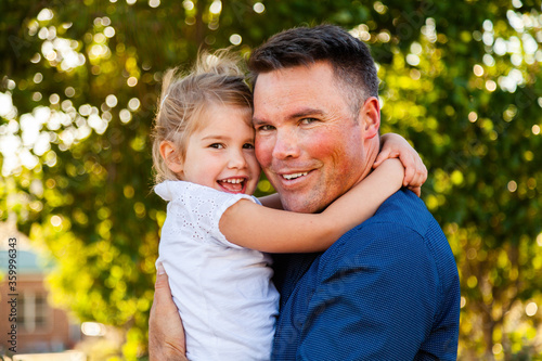 Portrait of a smiling father hugging his happy daughter in golden sunlight photo