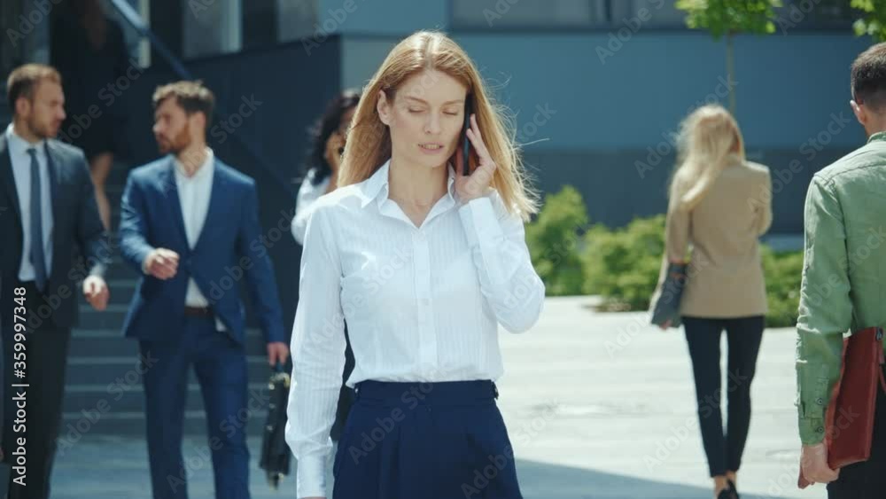 Beautiful blonde businesswoman leader executive boss talking with business partner on mobile phone. Busy business corporate people walking on street outdoors.