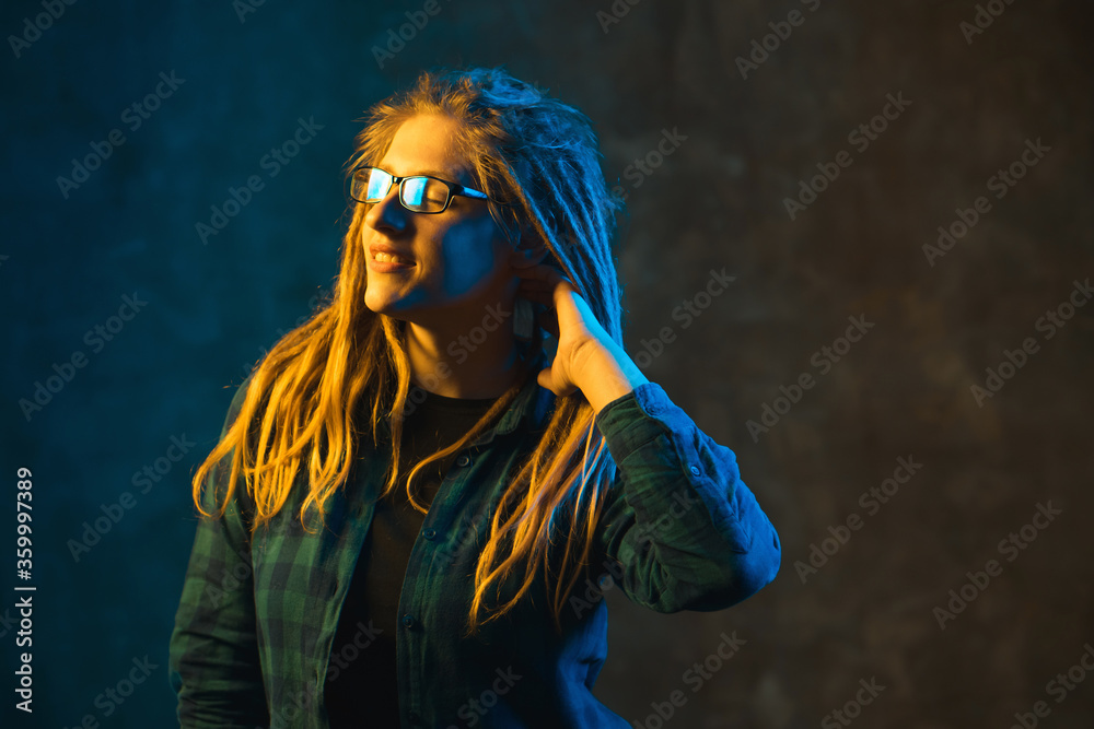 Young woman with dreadlocks in colorful neon lighting. Stylish attractive girl in glasses on dark background. Young woman with dreadlocks in colorful neon lighting. Stylish attractive girl in glasses on dark background.
