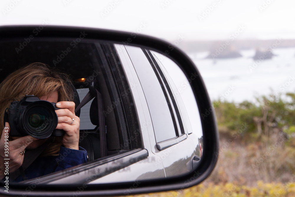 Woman taking a picture of self in car side rear view mirror
