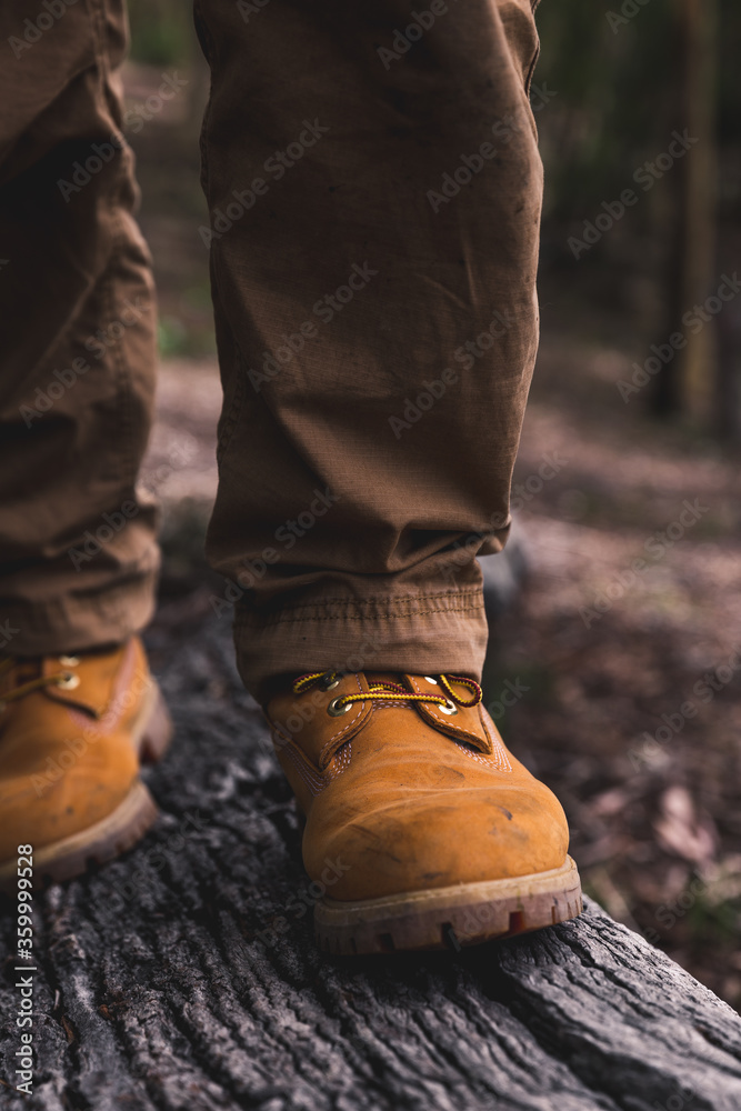 Man walking in yellow boots across fallen log in bush Man walking in yellow boots across fallen log in bush