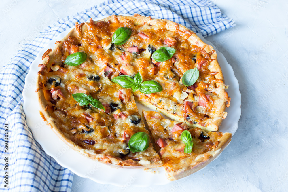 Delicious and crispy pizza with olives and sausages with a cut piece on a light background with a blue napkin, top view, copy space
