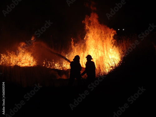 Firefighters fighting a grass fire at night silhouetted against the fire