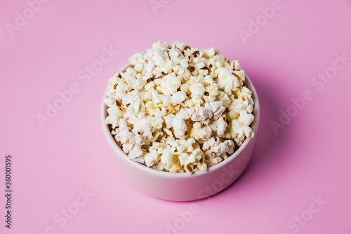 A pink bowl of popcorn on pink background, top view
