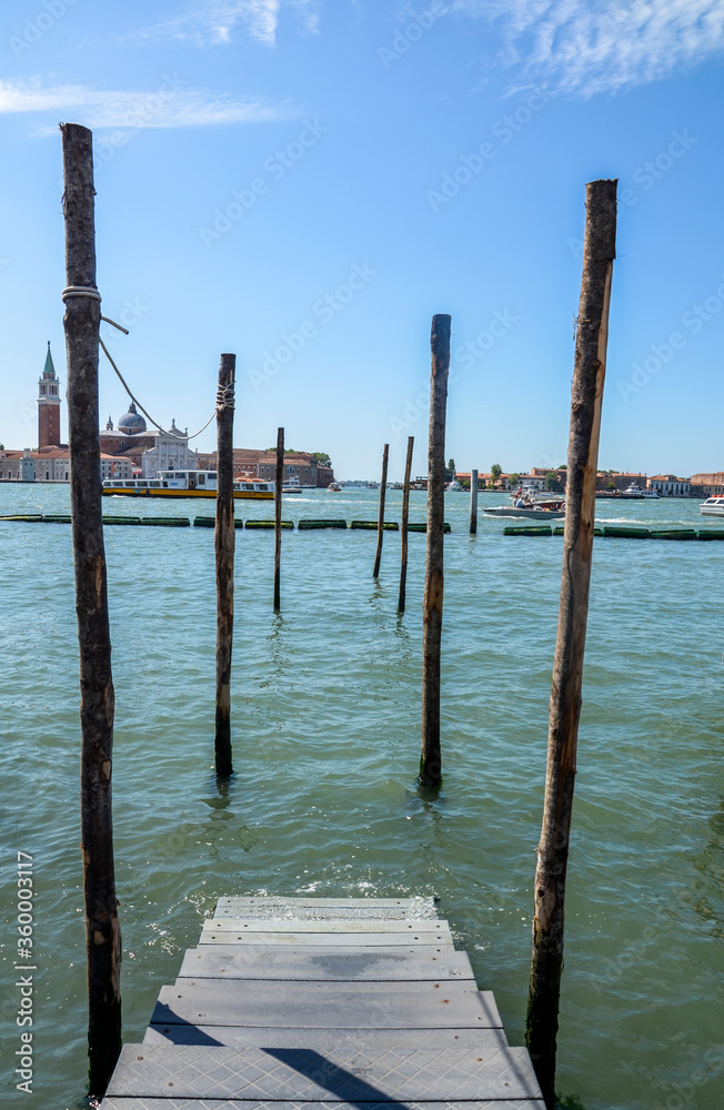 Landscape of gondolas marina with wooden beams of mooring posts in the water canal  and San Giorgio Maggiore island on background in Venice, Italy