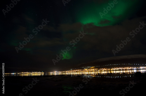 aurora borealis, northern lights over snowy mountain, reflective fjord water and whale island in northern norway in late autumn