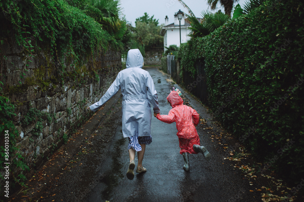 Woman and little girl running in rain coats in the street in France
