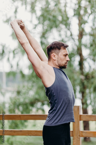 Flexible man in t-shirt rises haund up, bent back and stretches on a nature. photo