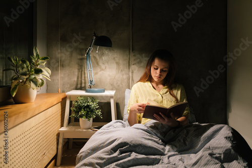 Young woman reading a book in bed photo