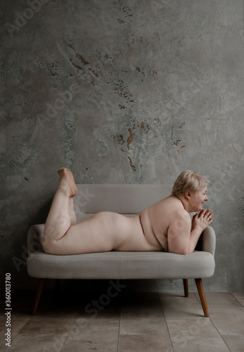 Naked woman with overweight lying on stomach on sofa.