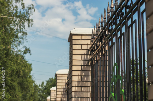 Beautiful fence made of bricks and metal bars on a sunny summer day. Walk around the Russian city.