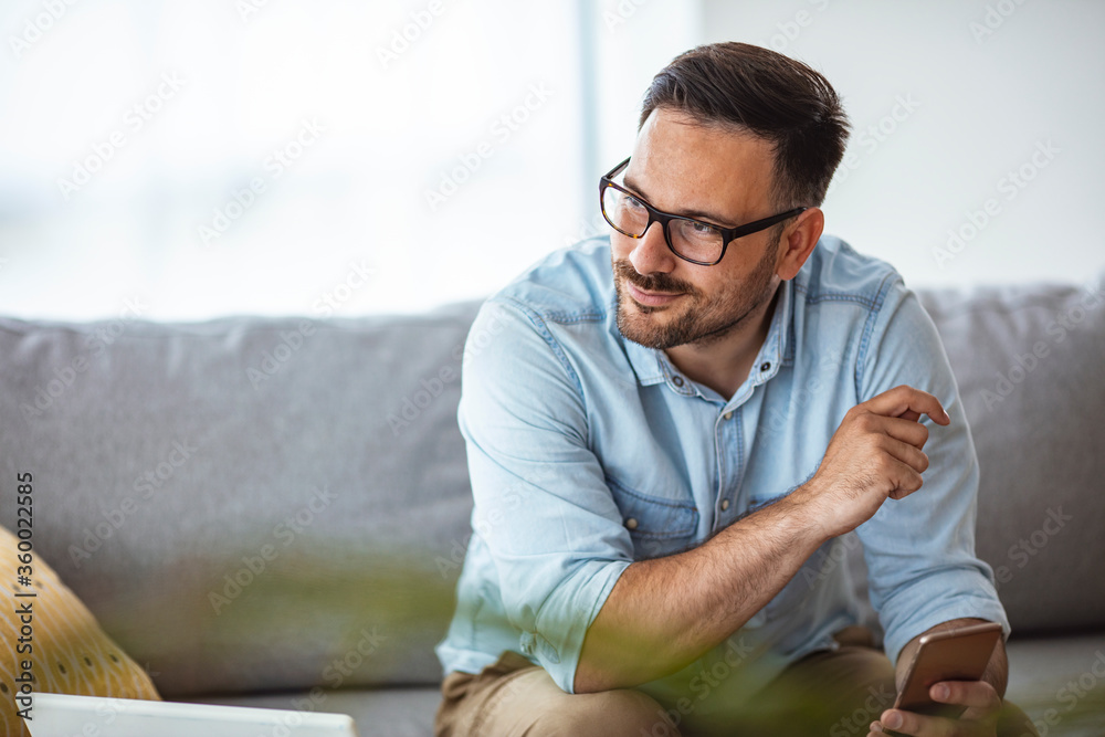 Shot of a young man using a smartphone on the sofa at home. What's the vibe on the newsfeed. Businessman holding smartphone for checking work or make appointment Shot of a young man using a smartphone on the sofa at home. What's the vibe on the newsfeed. Businessman holding smartphone for checking work or make appointment