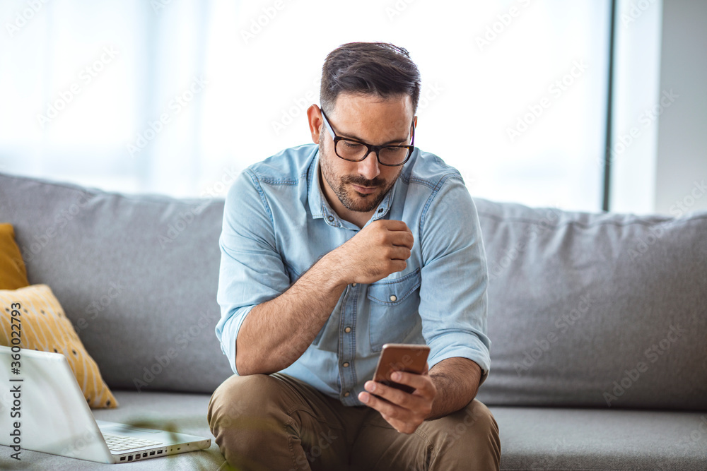 Man with spectacles relaxing sitting on couch while looking at mobile phone. Closeup of mature man using smartphone to checking email at home. Man reading email on smartphone
