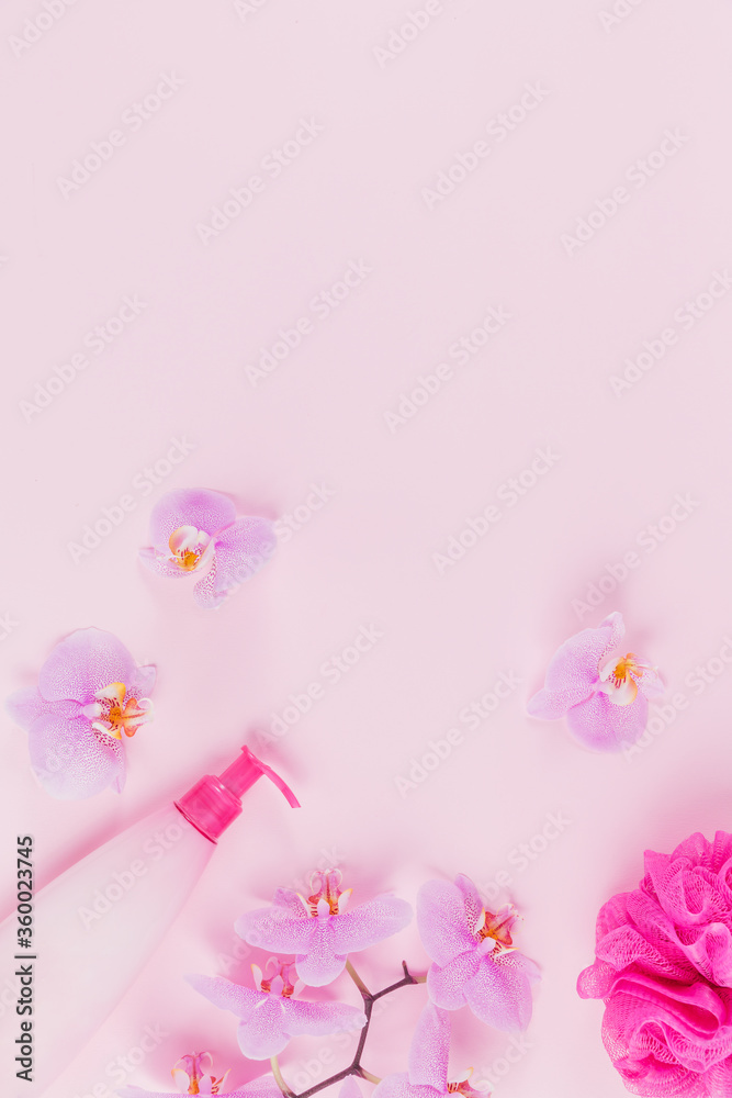 Plastic dispenser bottle with cosmetic soap, shampoo or shower gel, pink sponge and purple orchid flowers on pink background. Spa and wellness concept Plastic dispenser bottle with cosmetic soap, shampoo or shower gel, pink sponge and purple orchid flowers on pink background. Spa and wellness concept