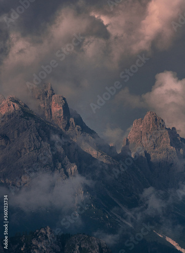 Dramatic view of mountain peaks wrapped in clouds at the golden hours of sunset in the Dolomites, South Tyrol, Italy.