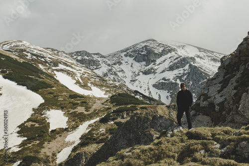 Man in front of high mountain landscape. Guy posing with rocks and mountains on the background.