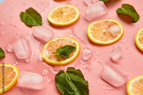 Composition with cut citrus fruits on pink background. Creative summer background composition with lemon slices, leaves mint and ice cubes. Minimal top down lemonade drink concept.Top view