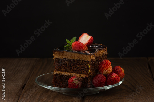 A slice of cake with strawberries on a glass plate against a dark background. photo