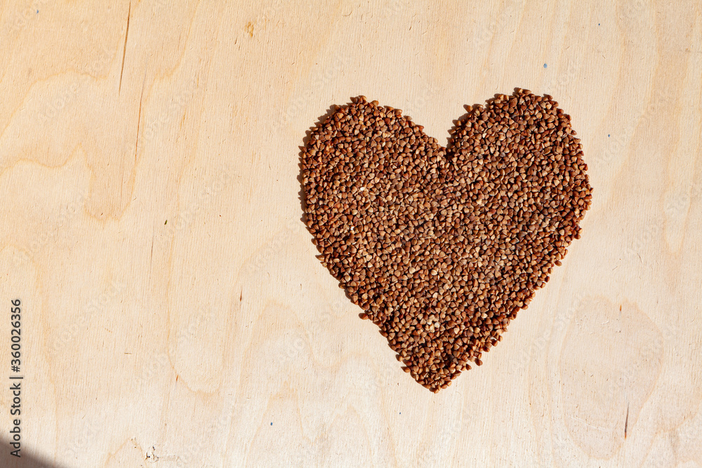 Buckwheat heart on wooden background with place for an inscription. Heart symbol made from buckwheat. Heart made of cereals. Healthy eating