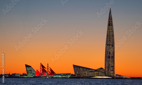 A ship with red sails at sunset on the background of a beautiful city and a skyscraper