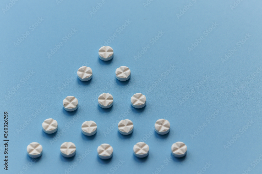 Round tablets of white color are laid out in the form of a triangle on a blue background. Close up Round tablets of white color are laid out in the form of a triangle on a blue background. Close up
