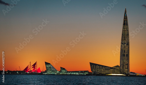 A ship with red sails at sunset on the background of a beautiful city and a skyscraper