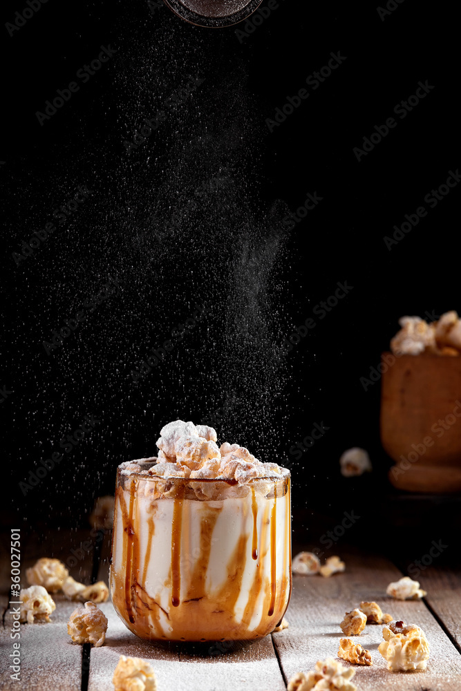 Milkshake with popcorn and caramel syrup on a black background. Sprinkle with powdered sugar.