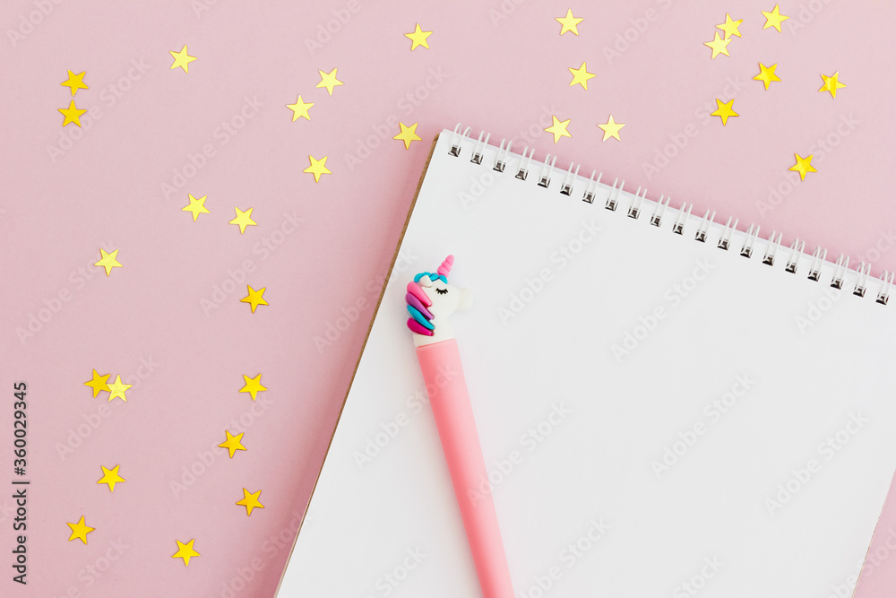 Notepad and unicorn pen on a pink background with golden star confetti. Setting goals for the year. The concept of making wishes. Layout, top view. Notepad and unicorn pen on a pink background with golden star confetti. Setting goals for the year. The concept of making wishes. Layout, top view.