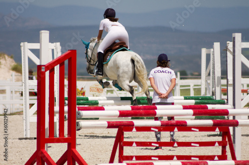 Female horse jumper being observed by her coach on a training session.
