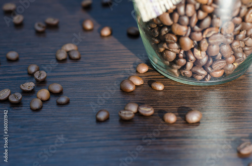 Coffee grains on a brown wooden table in the rays of sunlight. Part of a transparent can with coffee beans on the table. The sun shines on the grains of coffee.