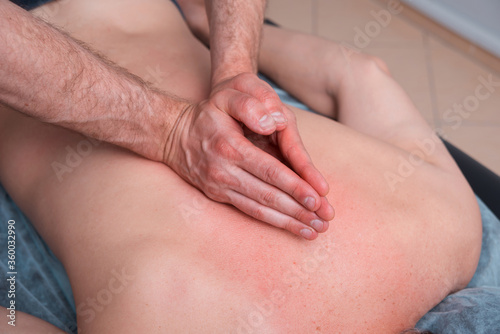Male Physical therapist is pressing on one mans back with both hands together.