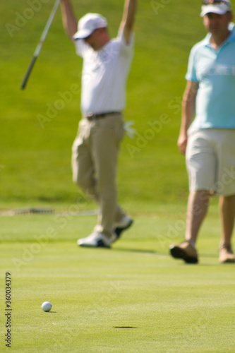 Valdeolmos, Madrid, Spain. Male player hits the ball from the tee into the hole and misses while other player raises hands in sign of victory.