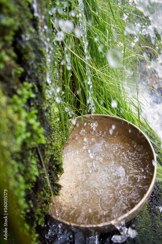 Tibetan singing bowl under a waterfall with water and moss in the background.