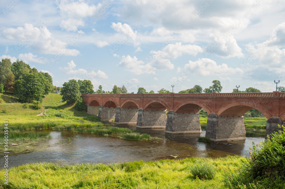 landscape view with old ancient red brick bridge with arches over the Venta river in Kuldiga, Latvia