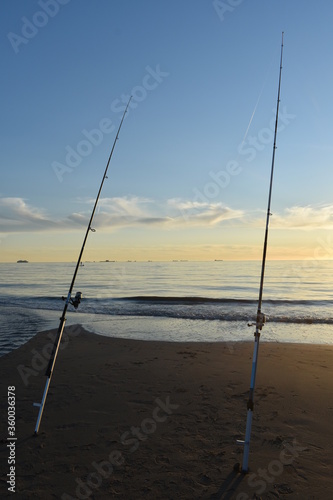 Fishing rods with reflections on cast lines on the beach at Katwijk aan Zee The Netherlands at sun set.