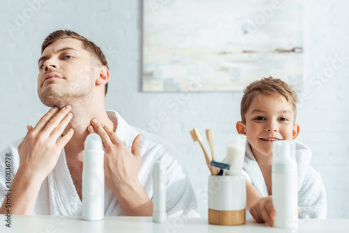 selective focus of serious man touching face near smiling son in bathroom