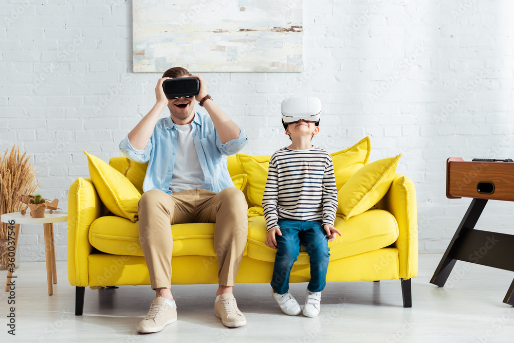 Fotografie excited father and son using vr headsets while sitting on yellow sofa