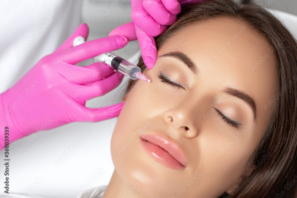 Beautiful brunette woman at the beautician.Cosmetologist does anti wrinkle injections around eyes and between eyebrows. Women's cosmetology in the beauty salon.