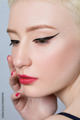 Portrait of a beautiful young woman with short blond hair  beautiful fresh makeup and healthy clean skin on a gray background. The concept of makeup and cosmetology.