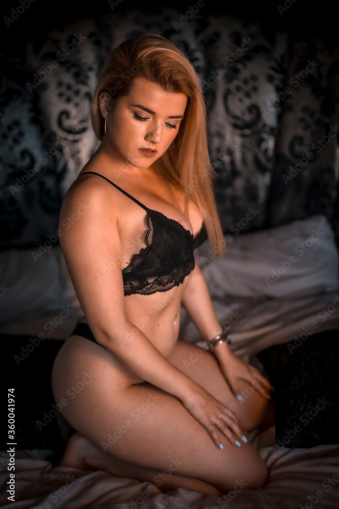 Boudoir session with a young blonde Caucasian woman on top of a bed with black lingerie, in a circular bed with a beautiful headboard of black flowers. Posing on her knees on the bed Boudoir session with a young blonde Caucasian woman on top of a bed with black lingerie, in a circular bed with a beautiful headboard of black flowers. Posing on her knees on the bed