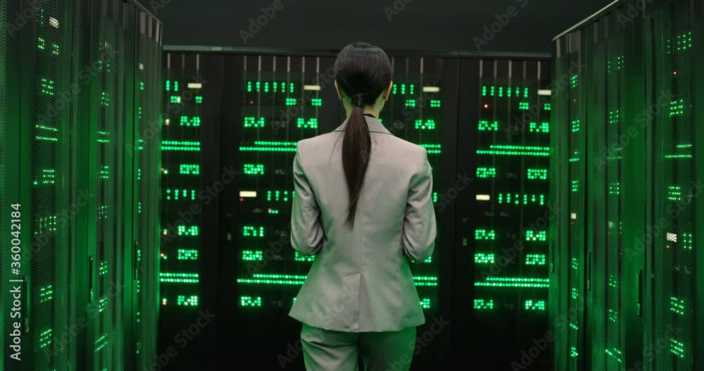 Rear of Caucasian young woman walking among servers with big data information. Green working processors in database storage. Back view on female worker of digital telecommunication. Analytics work.