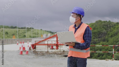 Construction engineer or an architect with a halmet and protective mask and equipment using a computer during COVID-19 virus. photo