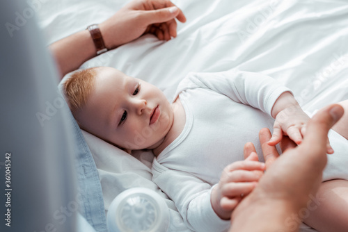 high angle view of adorable baby boy touching fathers hand while lying in bed