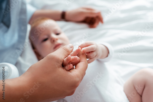 selective focus of adorable infant touching fathers hand while lying in bed