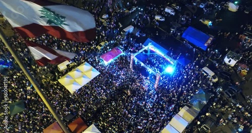 Beirut, Lebanon 2019: night lift up drone shot in martyrs' square, starting from protesters around a stage revolting against government passing by Lebanese flag in foreground during the revolution photo