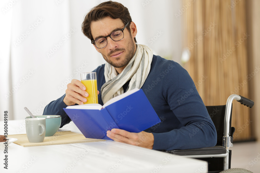 male teacher in wheelchair reading a book while having breakfast male teacher in wheelchair reading a book while having breakfast