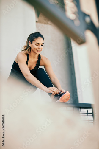 Young smiling attractive caucasian female runner tying shoelace and preparing for running.