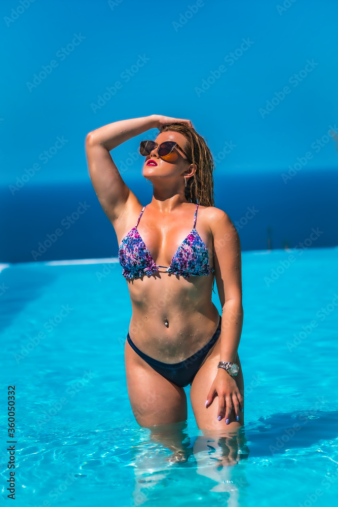 Summer lifestyle in an infinity pool with a young blonde Caucasian woman in a pink and purple bikini with sunglasses. Enjoying the pool on a hot summer afternoon Summer lifestyle in an infinity pool with a young blonde Caucasian woman in a pink and purple bikini with sunglasses. Enjoying the pool on a hot summer afternoon