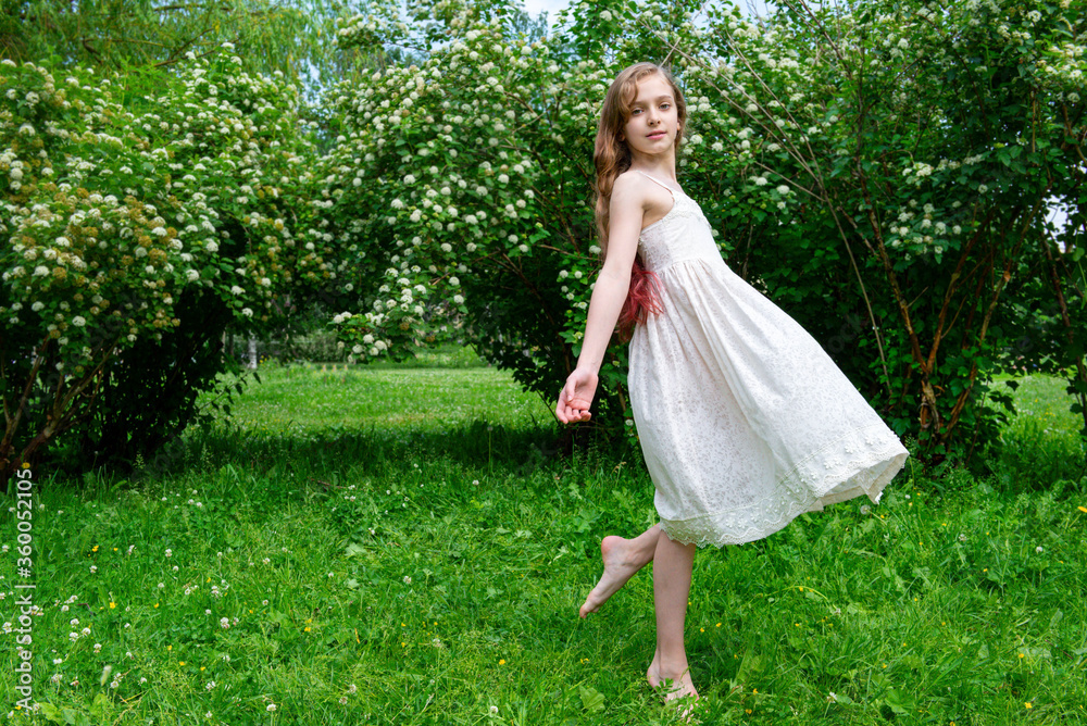 beautiful girl 11 years old with long hair in a white summer dress against a background of green bushes with white flowers beautiful girl 11 years old with long hair in a white summer dress against a background of green bushes with white flowers