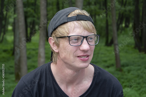 Street portrait of a young man in his 30s with glasses on the background of a forest.Perhaps he is a tourist or traveler, an office worker in nature.